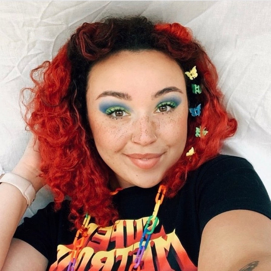 Model with Curly Cherry Red Hair – Smiling woman with curly cherry red hair, styled with colorful clips and vibrant makeup.