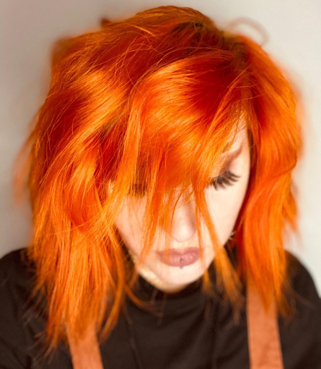 Woman with tousled, vibrant orange-dyed hair styled in a messy, edgy look, showcasing the bold color payoff of the dye.