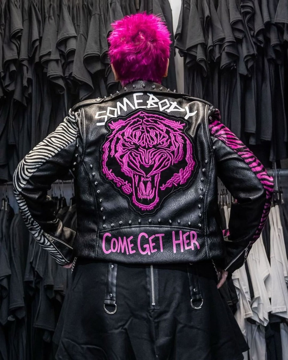 Person with a punk-inspired hot pink mohawk, wearing a black leather jacket with pink embroidered tiger and bold lettering.