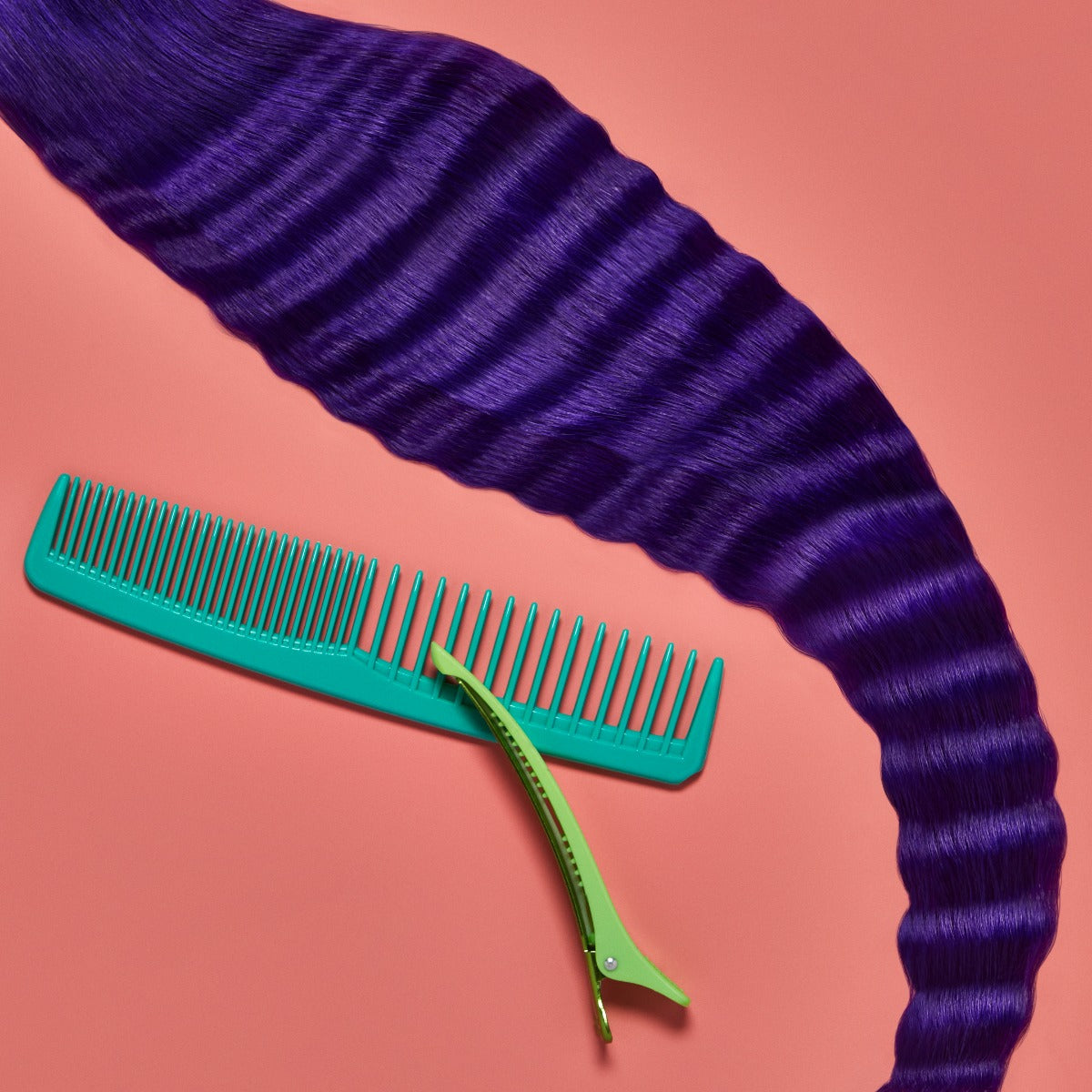 A section of wavy, bright purple hair on a muted pink background next to a a comb and hair clip, showcasing the Punky Colour Sugar Cloud Semi Permanent Foam Color