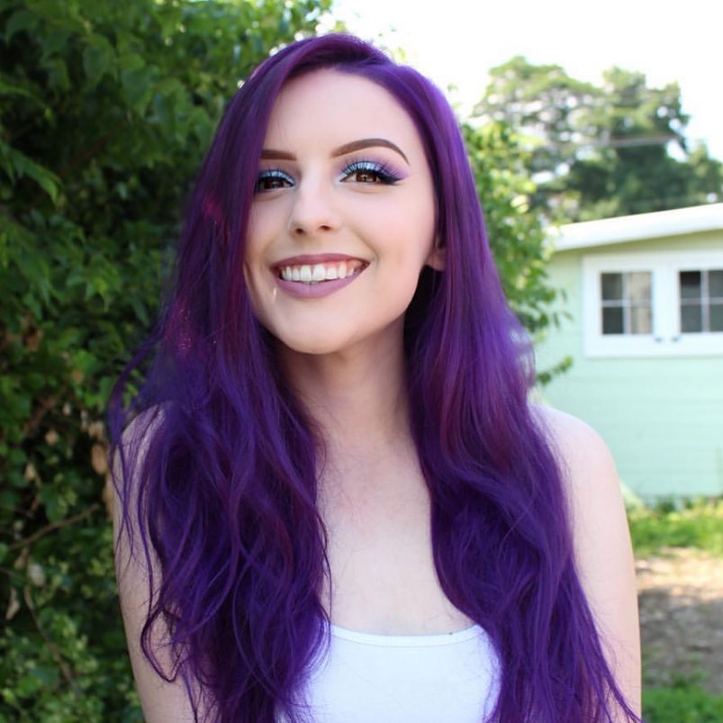 Woman with vibrant purple hair outdoors – A smiling woman with long, vibrant purple hair, styled in loose waves, enjoying an outdoor setting.